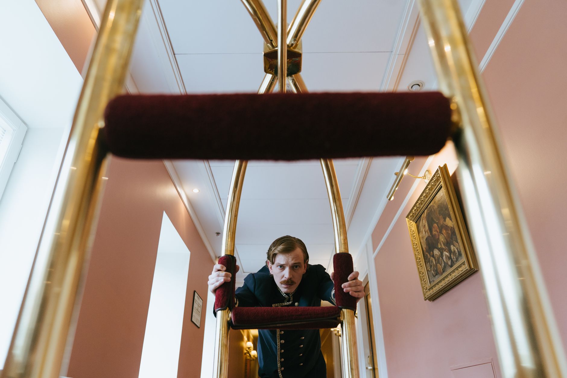 Hotel staff member in uniform pushing a luggage trolley through a corridor.