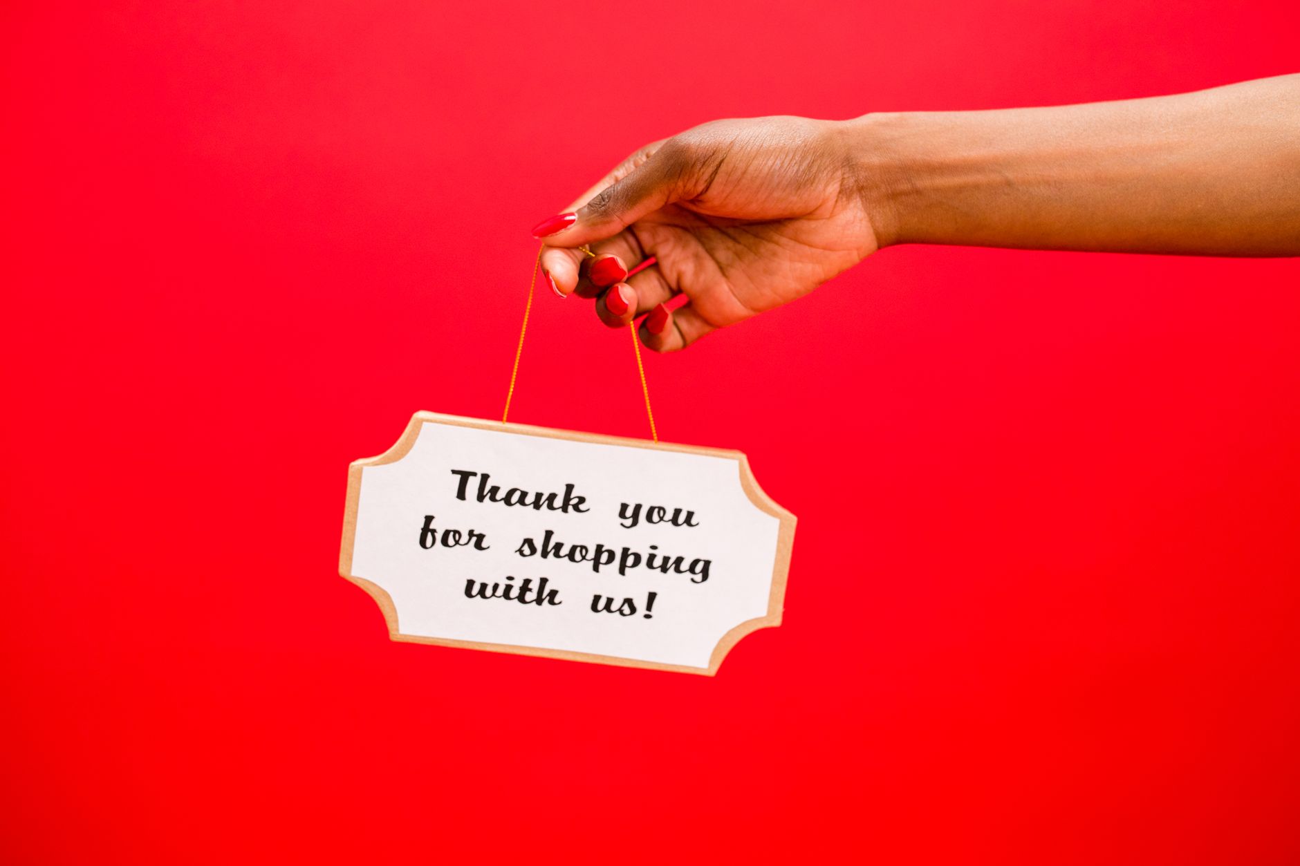 Female hand holding a sign saying 'Thank you for shopping with us!' against a vibrant red background.