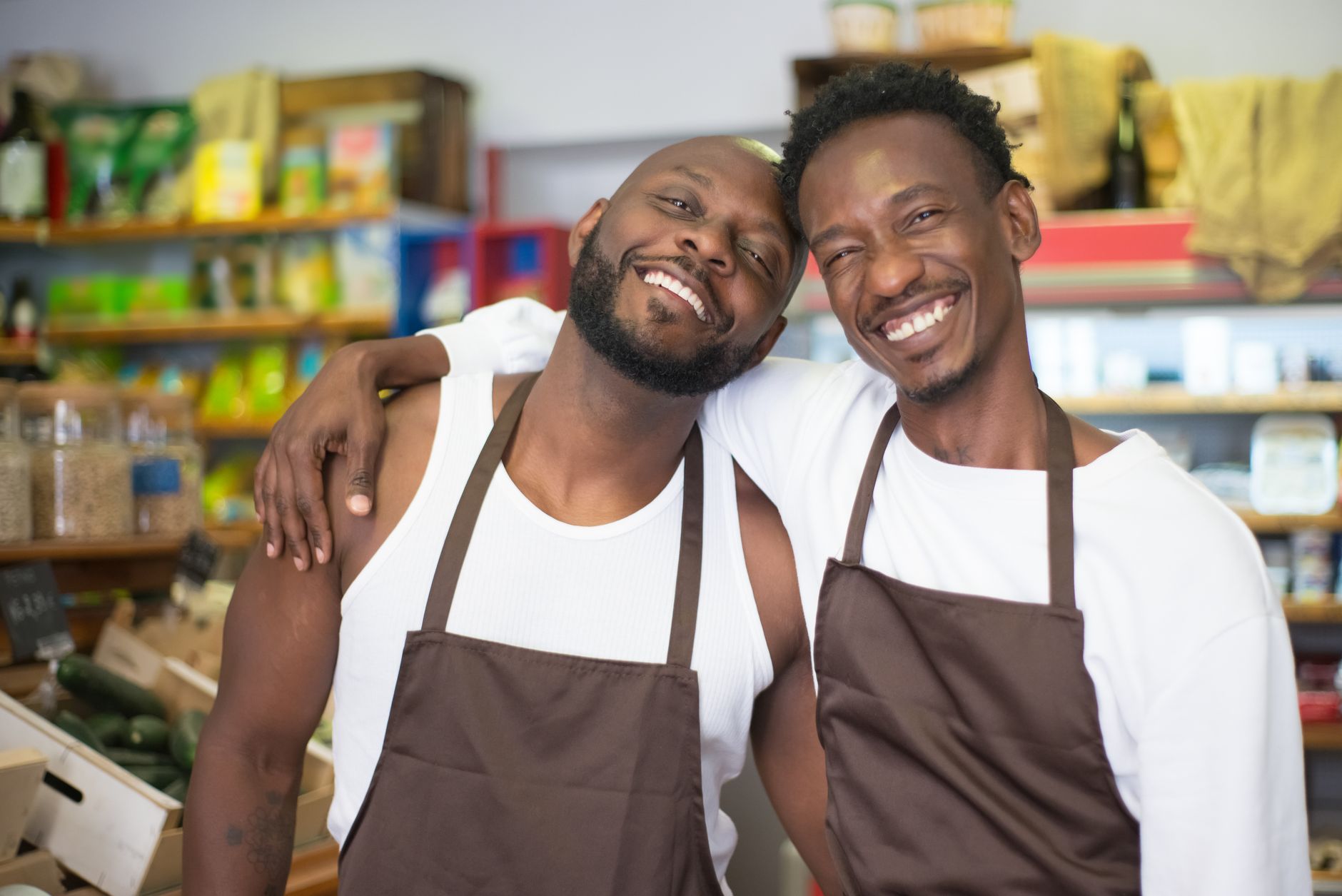 Smiling couple in aprons embracing in a grocery store. LGBT pride and happiness.