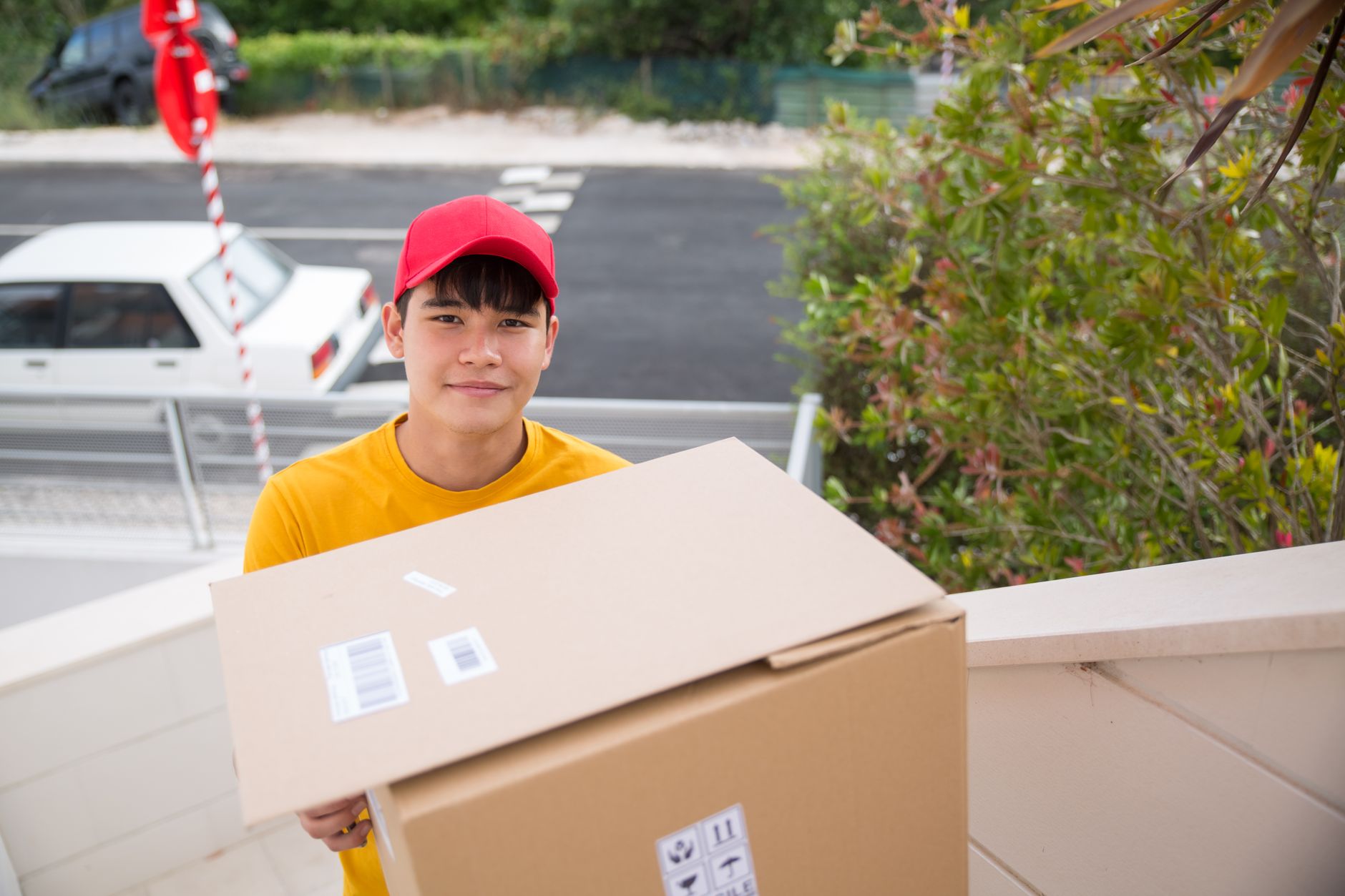 Delivery man with a cardboard box outdoors in Portugal, wearing a red cap and yellow shirt.