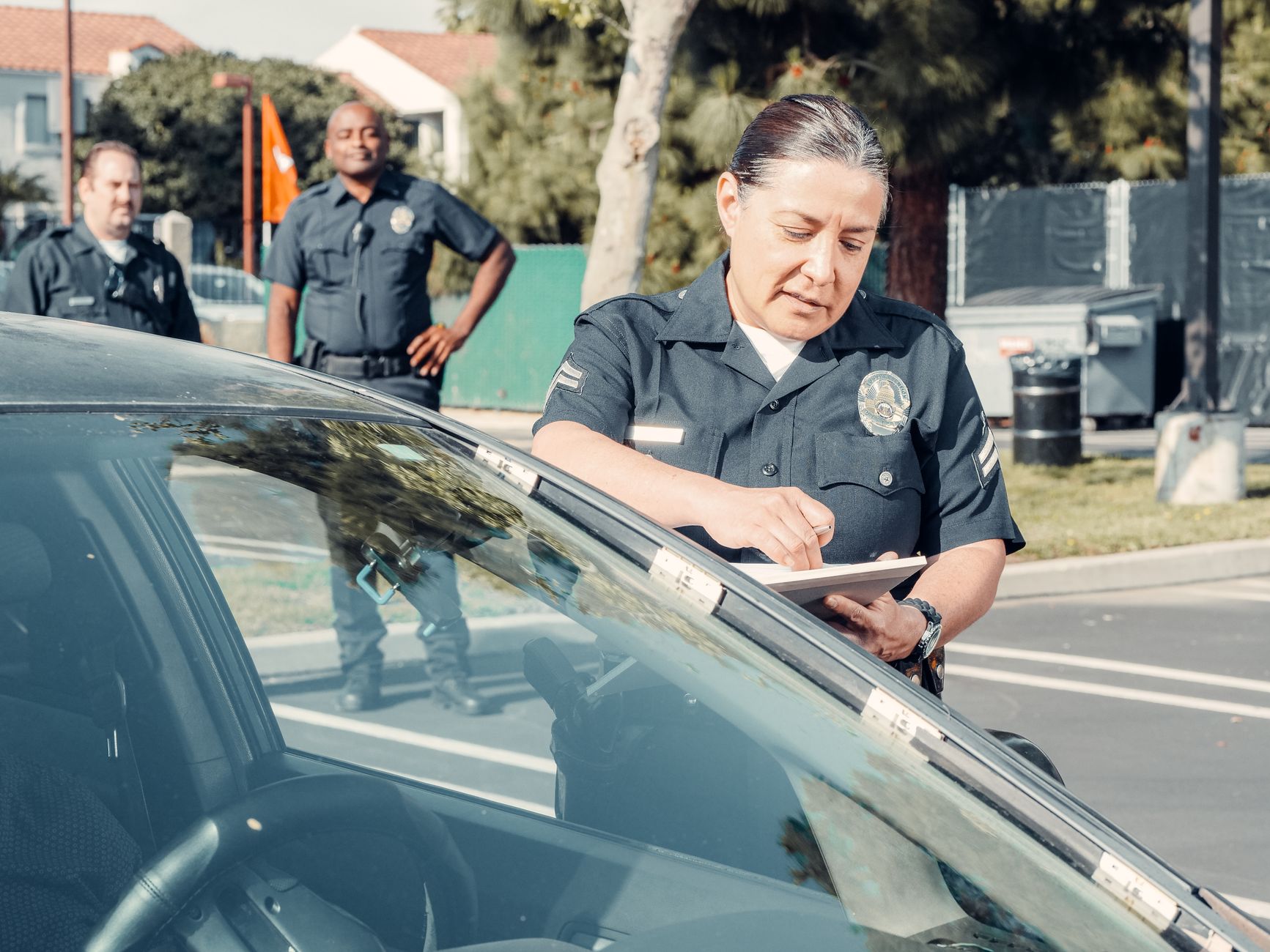Police officers handling a traffic violation in a parking lot, focus on policewoman writing a ticket.