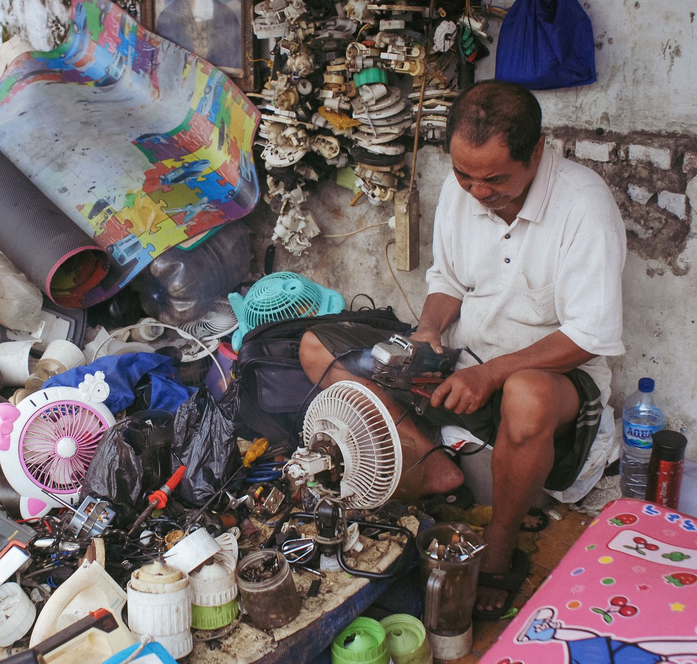 A street vendor in Jakarta, Indonesia, repairs electric fans amidst a colorful array of tools and parts.