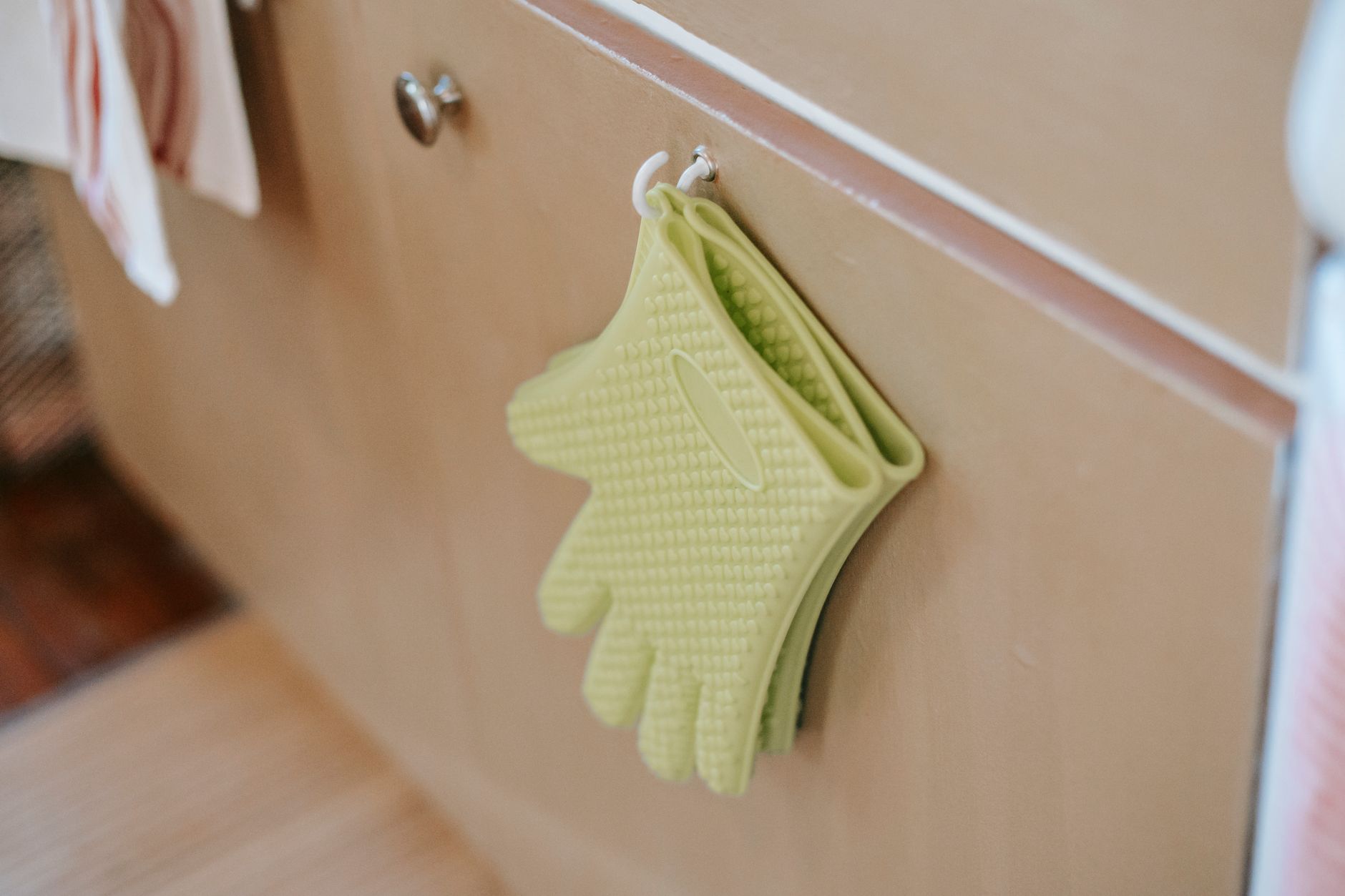From above of pair of potholders made of silicone with bumpy surface hanging on hook at home