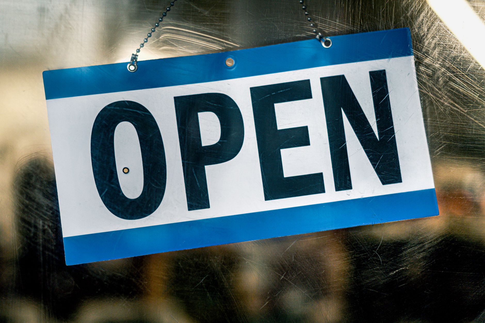 A blue and white open sign hanging on a retail shop's glass door.