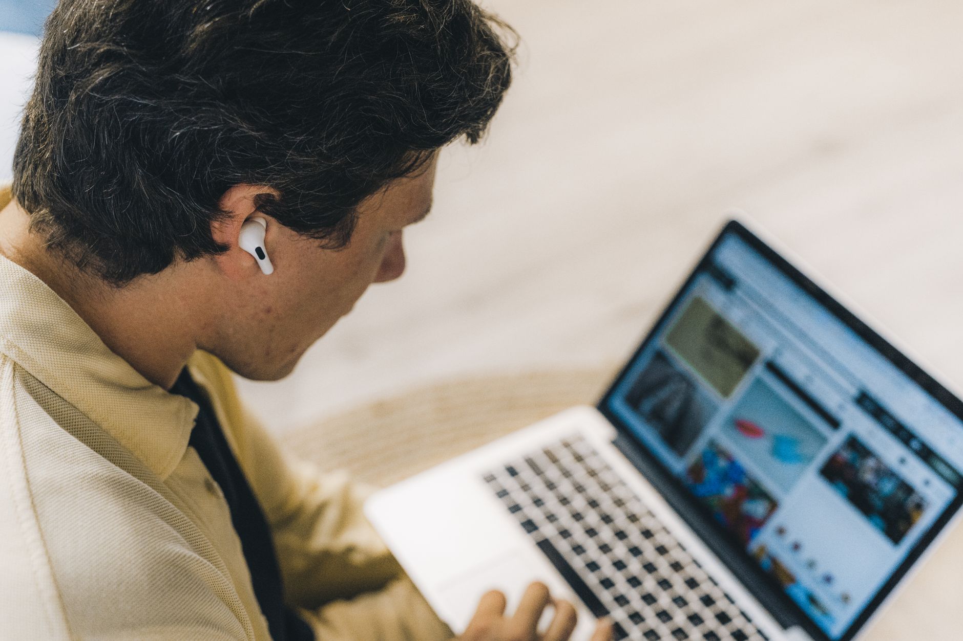 Man with earbuds working remotely on a laptop, embodying the digital nomad lifestyle, indoors.