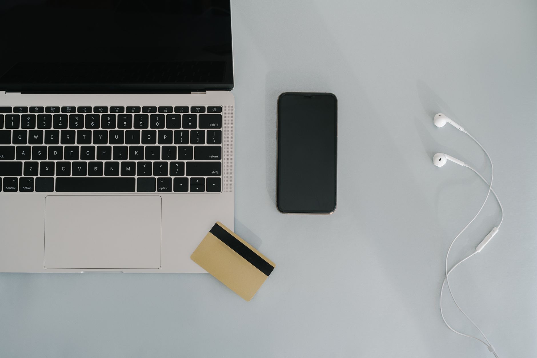 Flat lay of laptop, smartphone, and earphones with credit card on a desk.