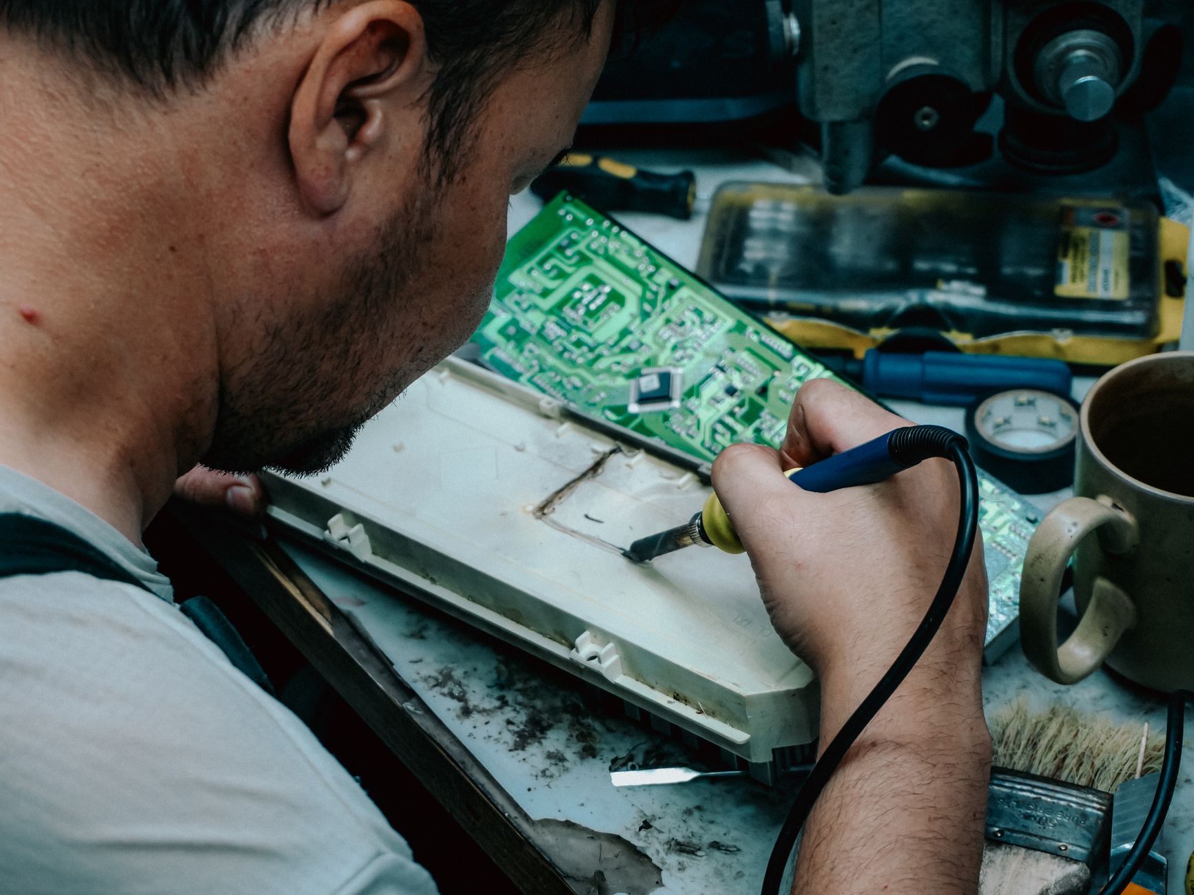 A focused technician using a soldering iron to repair electronic components at a workstation.