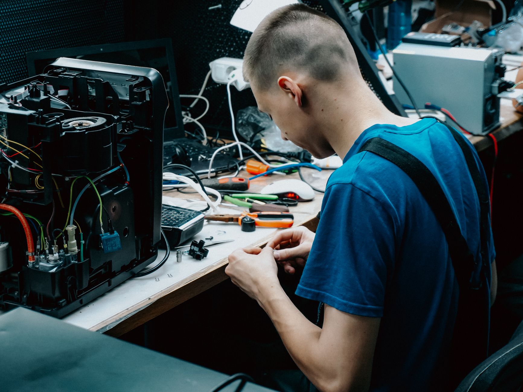 Skilled technician seated at a workbench repairing electronic devices in a workshop setting.