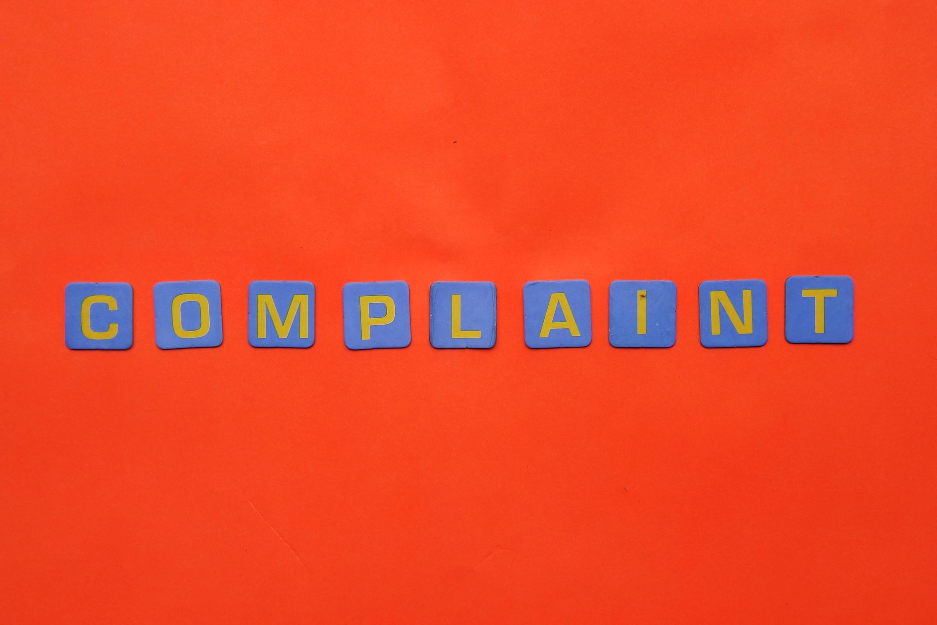 Blue letter tiles spelling 'COMPLAINT' on a vibrant red surface.