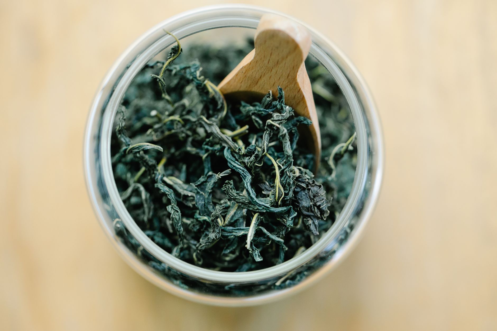 High-angle shot of dried tea leaves in a glass jar with a wooden scoop, perfect for herbal infusion themes.