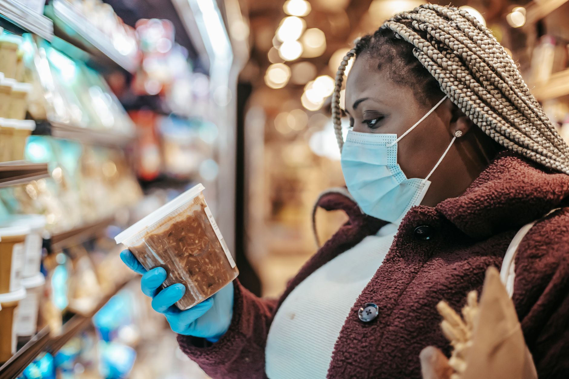 Side view of African American female customer on medical mask reading label on frozen food while shopping in grocery store