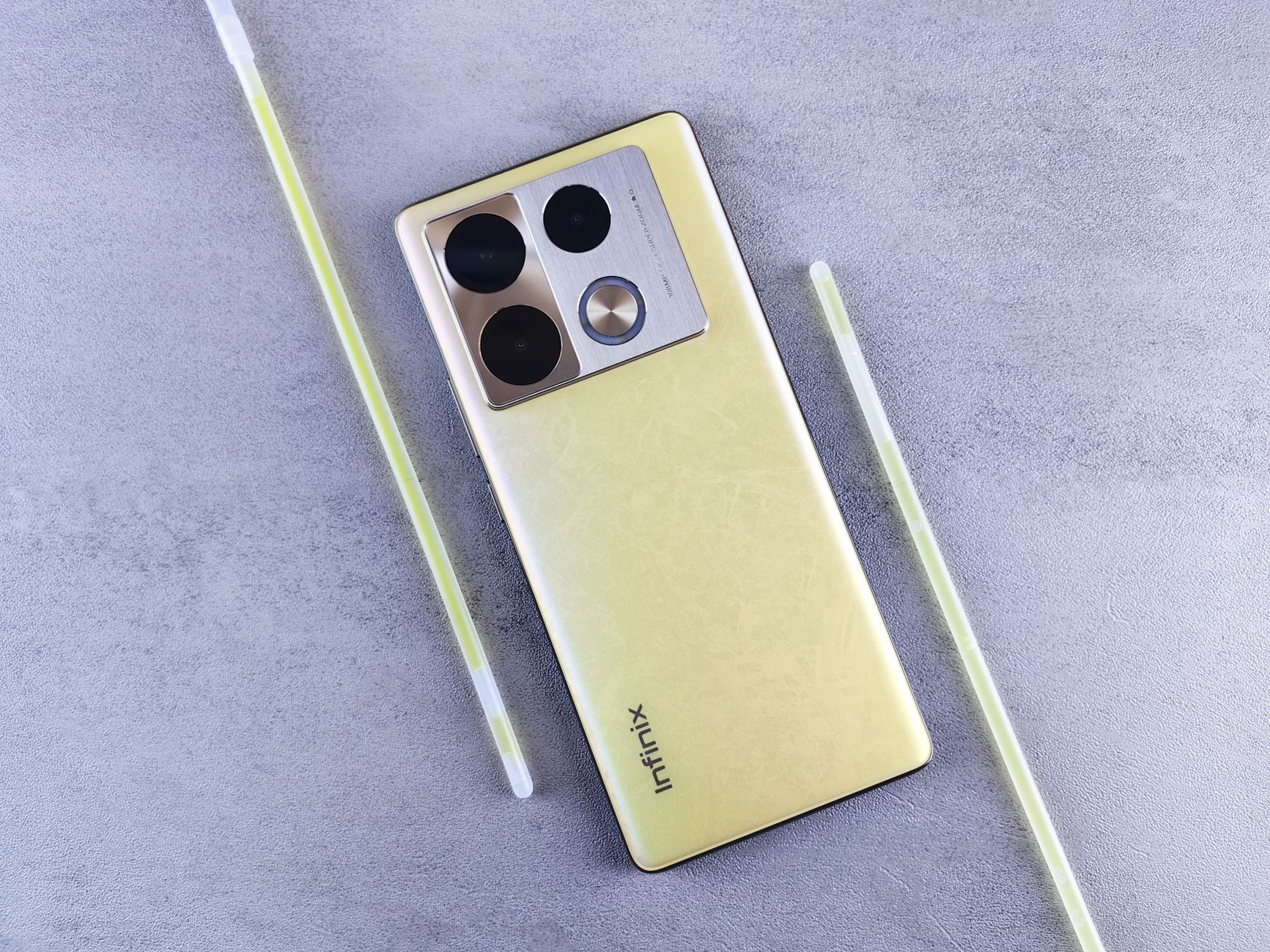 Capture featuring a gold Infinix smartphone on a gray textured backdrop, showcasing its camera module and elegant design.
