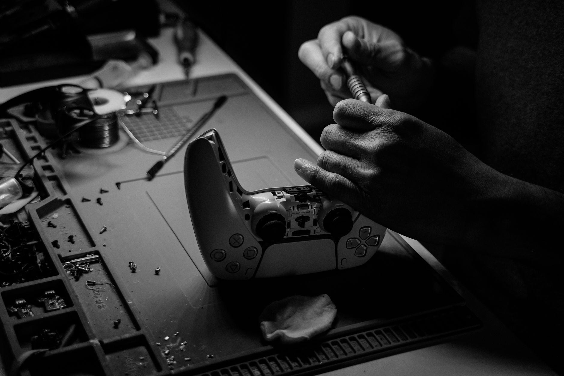 Close-up black and white image showing hands repairing a game controller at a workbench.