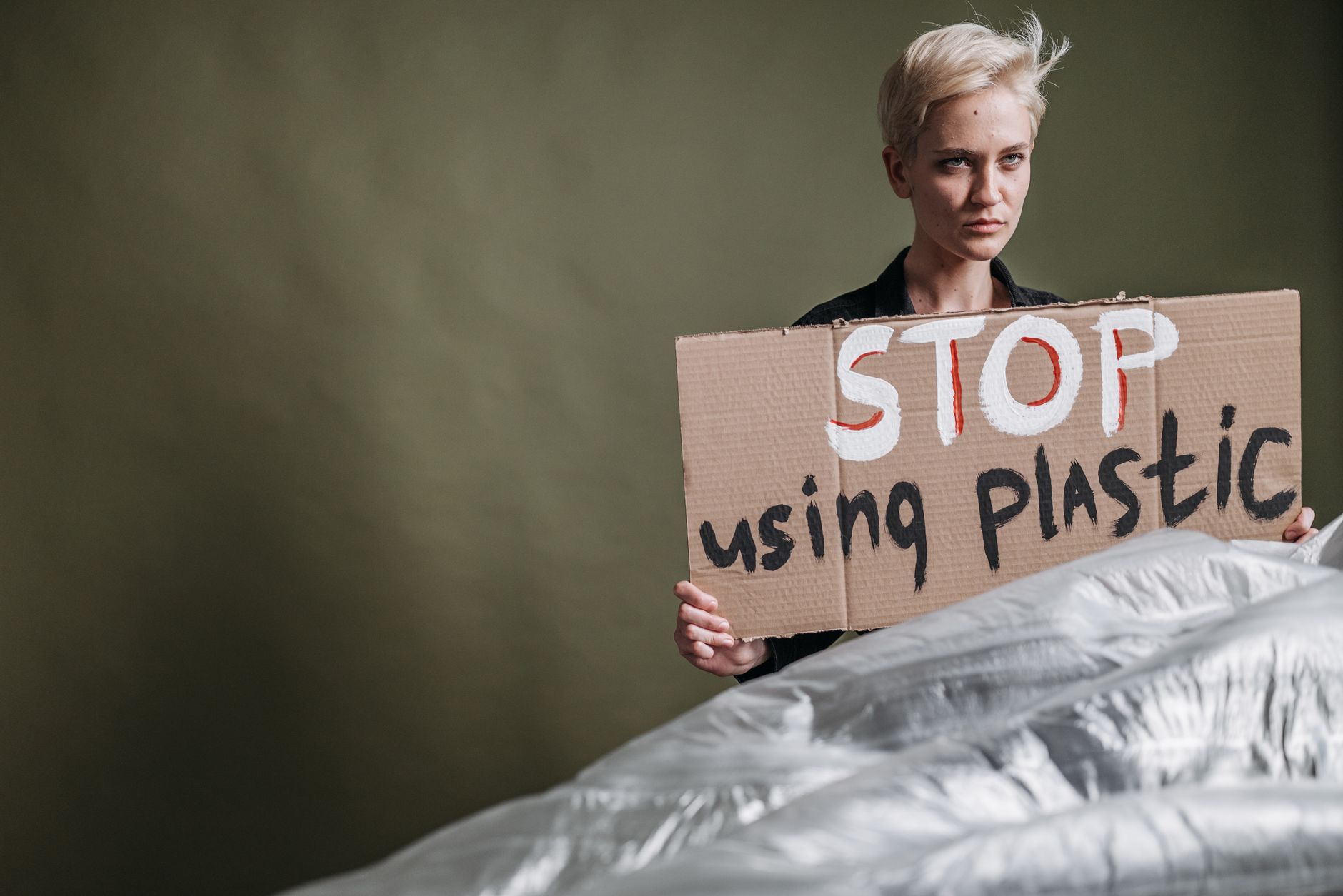 Portrait of an adult woman holding a sign urging to stop plastic usage.