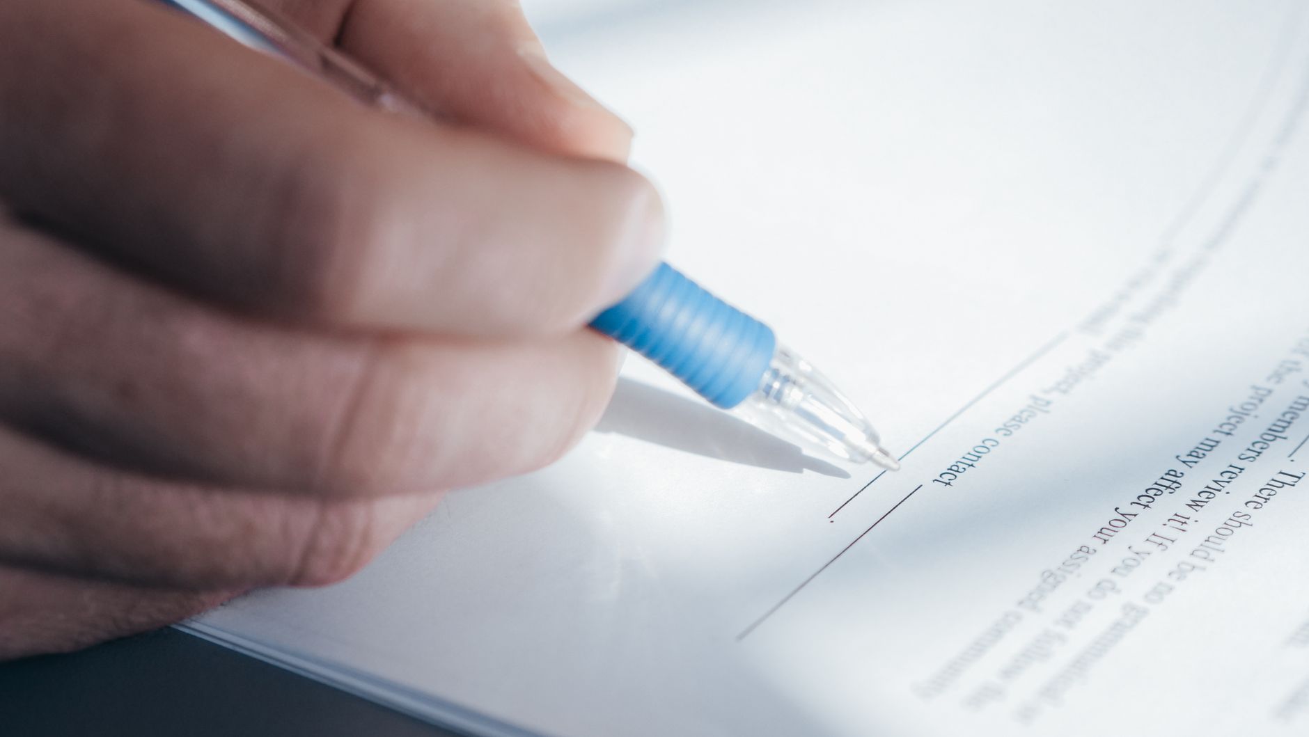 A close-up image showing a hand holding a pen while signing a document.