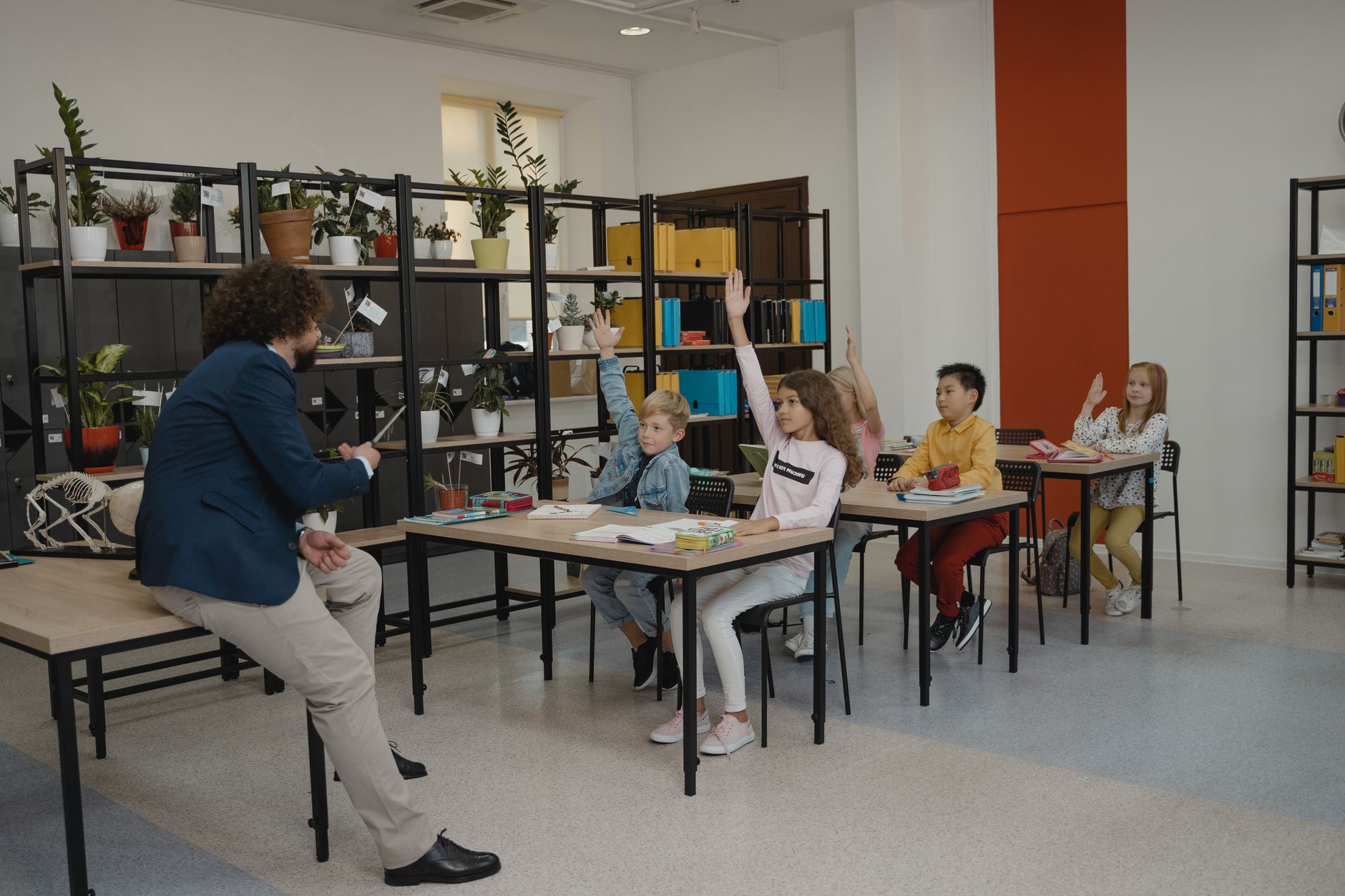 Students actively participating by raising hands in a modern classroom with attentive teacher and organized environment.