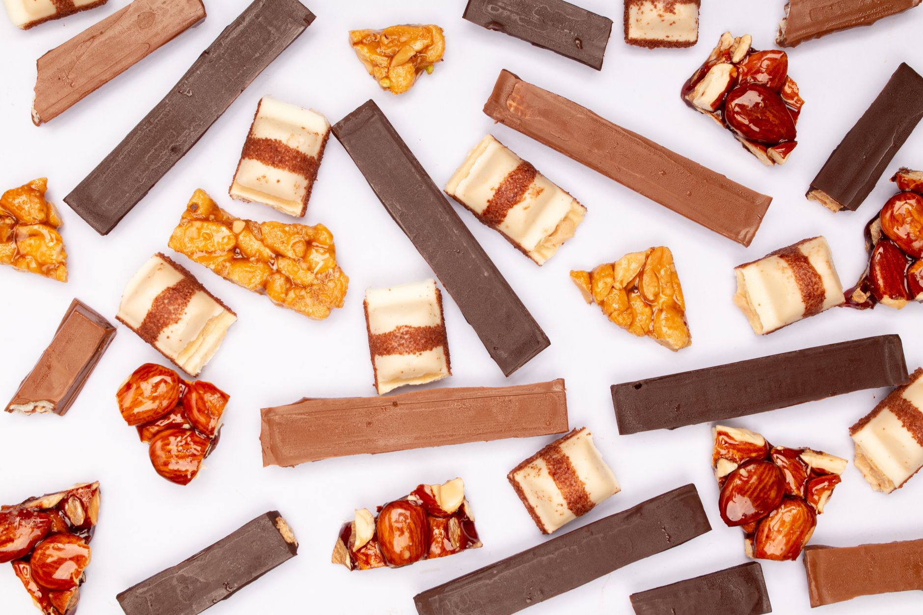 Flat lay of assorted chocolate and nut candy bars on a white surface, showcasing variety and texture.