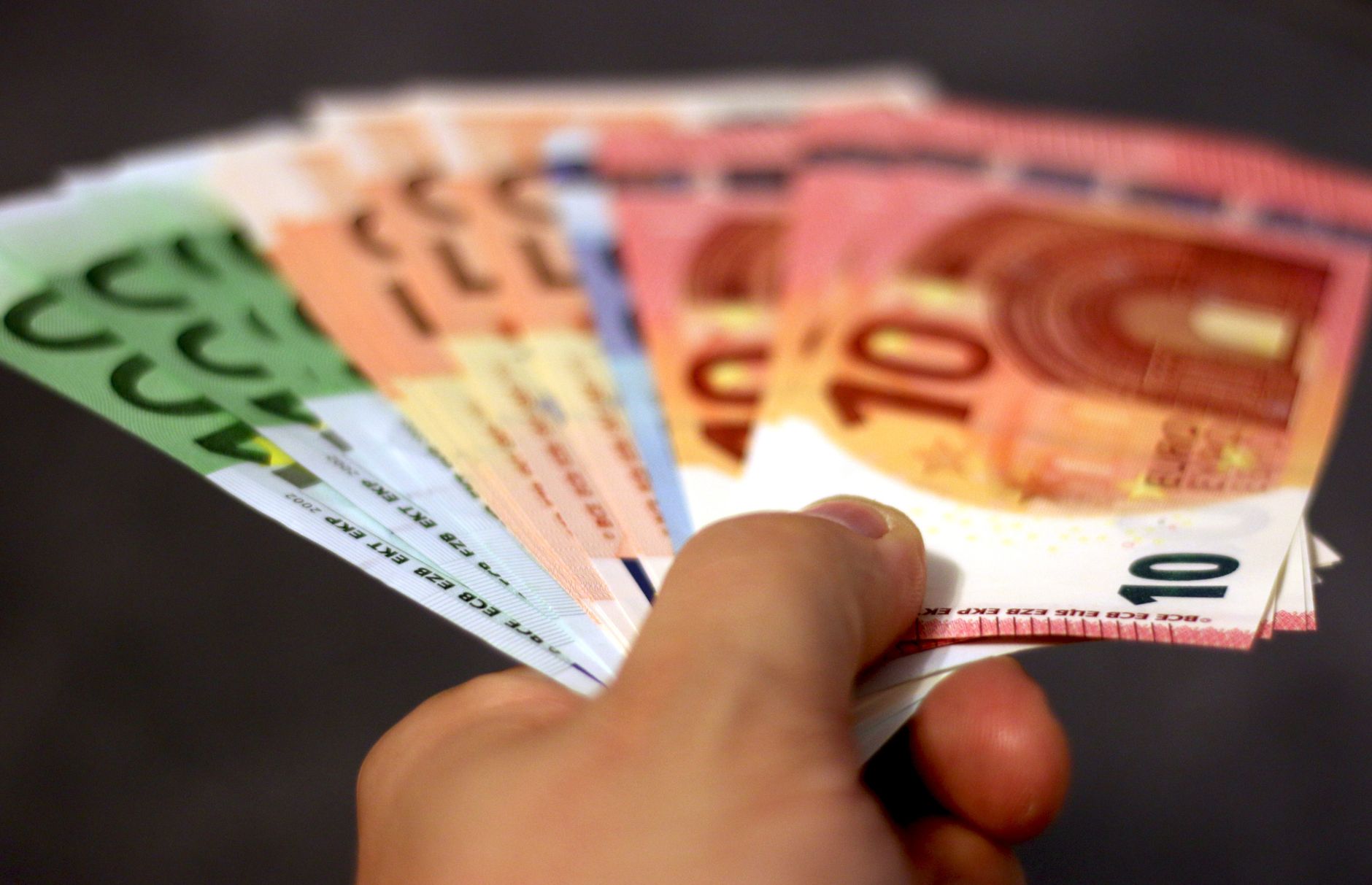 A close-up shot of a hand holding a fan of euro banknotes, symbolizing wealth and currency exchange.