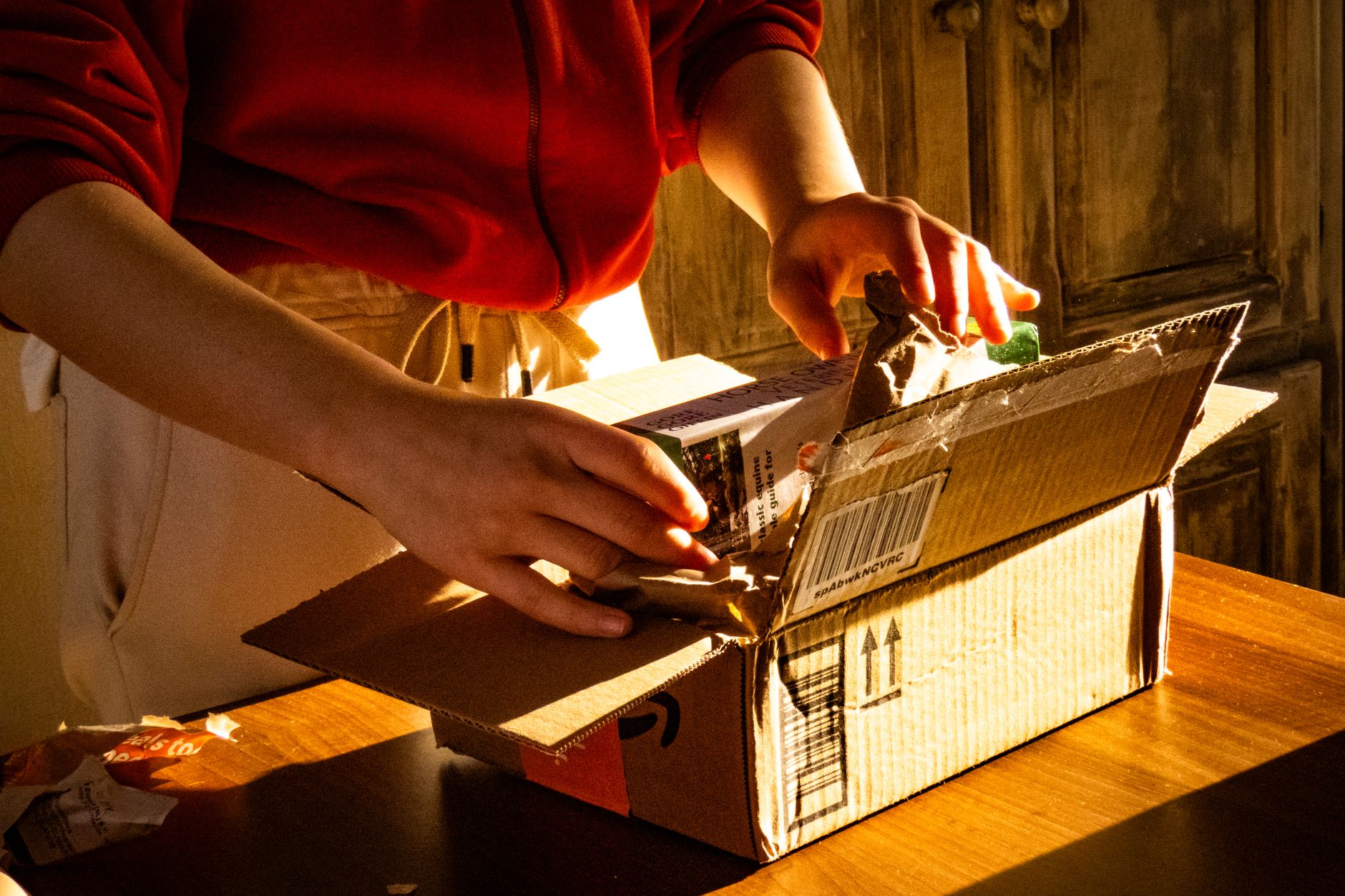 A person unboxing a package, revealing curiosity and anticipation in a warmly lit setting.