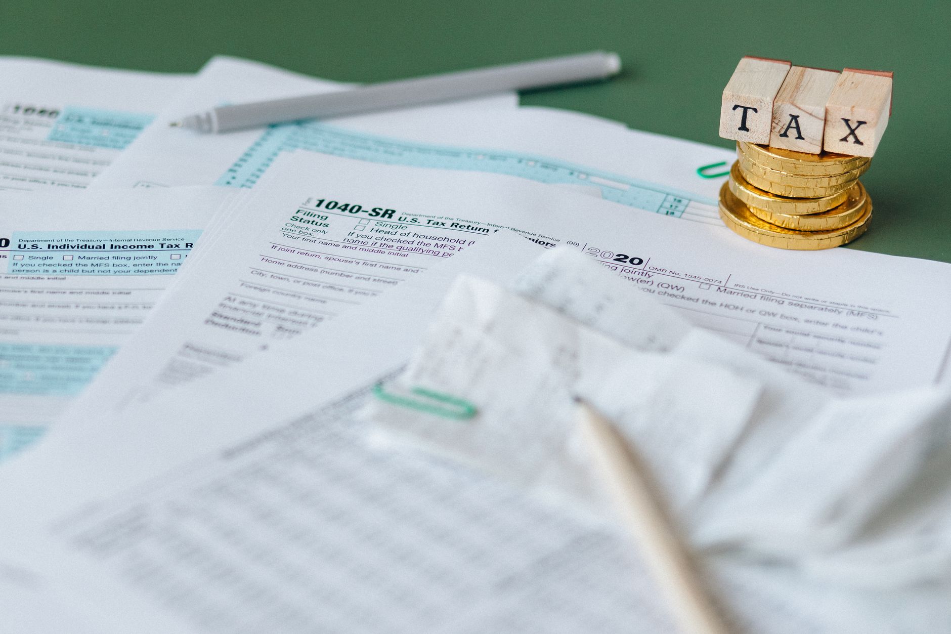 Stack of tax forms and coins with a 'TAX' stamp, symbolizing finance and accounting.