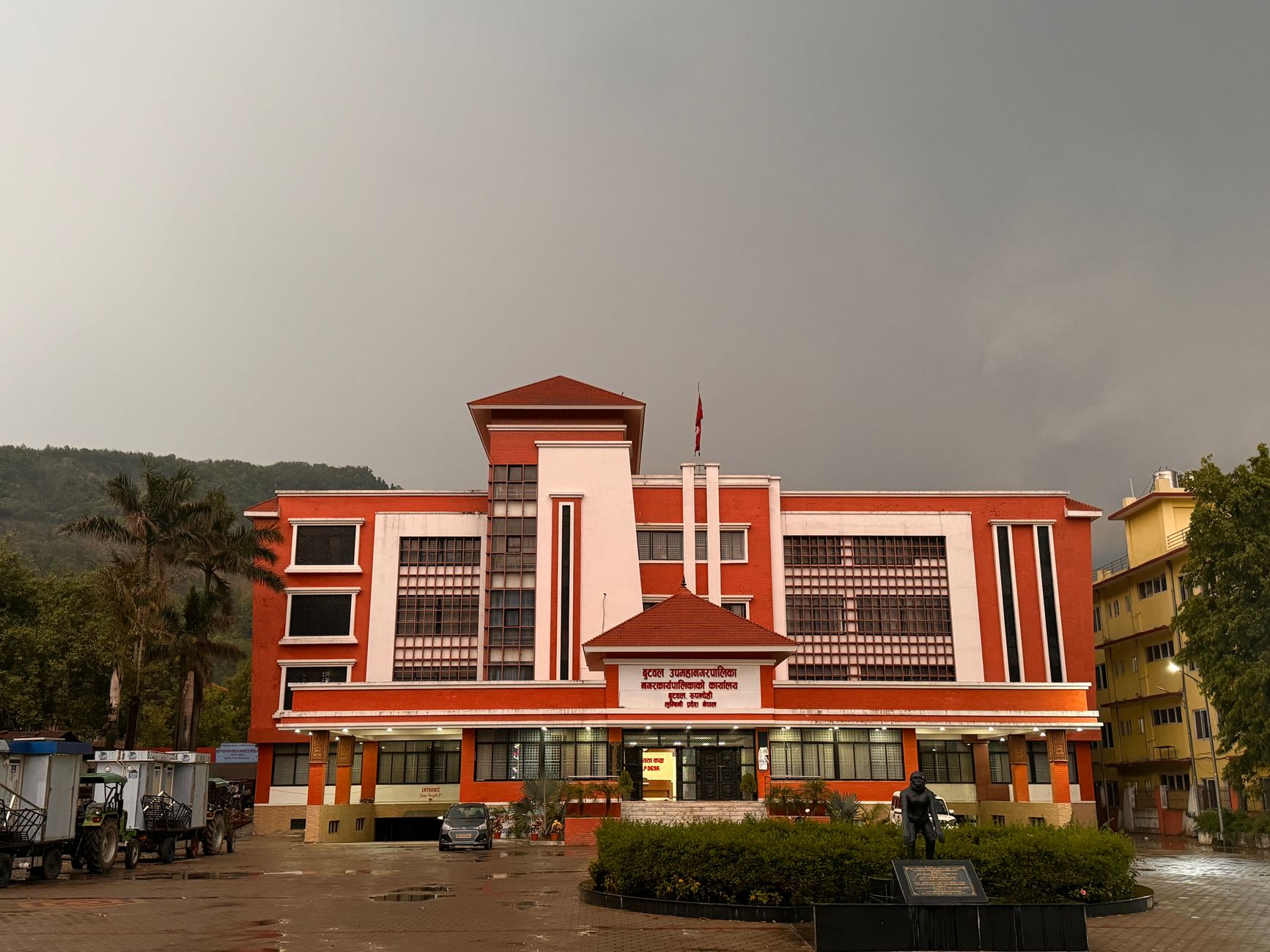 A striking red government building stands under an overcast sky, featuring modern architecture.